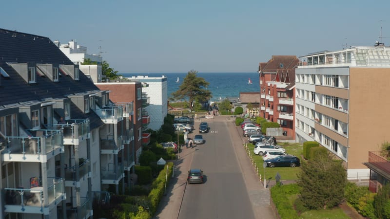 Aerial view flying between building street facing Baltic clear blue sea water in Scharbeutz, Germany, dolly in, day