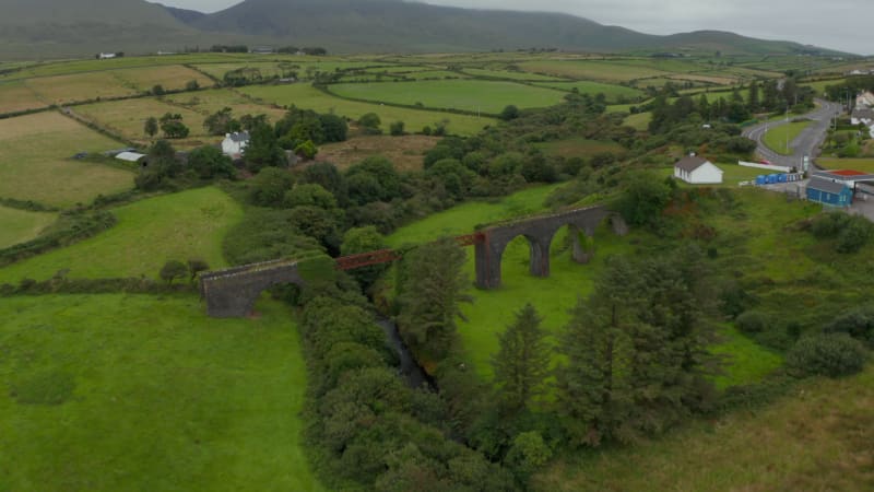 Fly over historic Lispole viaduct. Steel and stone construction of old railway bridge over valley. Tilt up reveal landscape panorama. Ireland