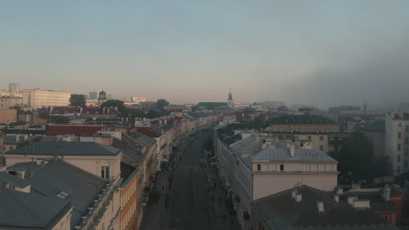 Misty morning in city. Forwards fly above street lined by town houses. Public transport buses driving on road. Warsaw, Poland