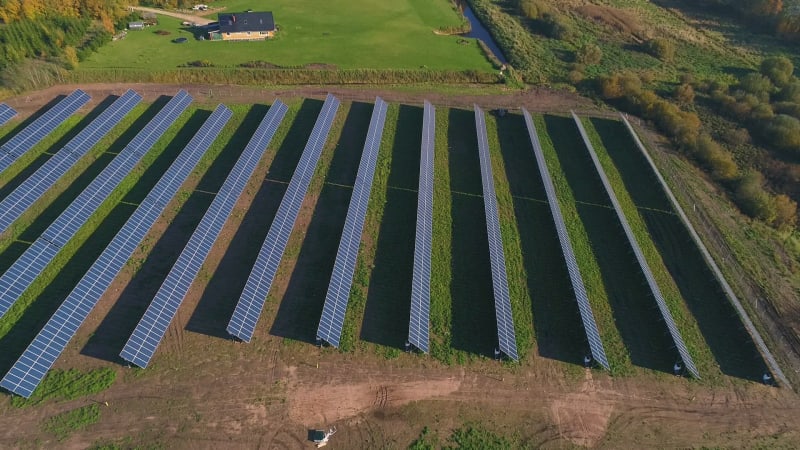 Aerial view of solar panel rows near a forest during Autumn.