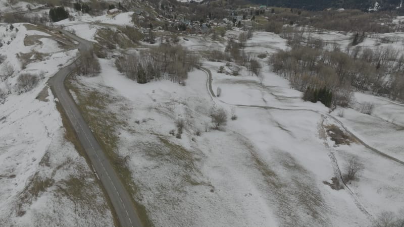 Forwards tilt up over a mountain road in lightly snow covered landscape in Les Sybelles, France in cloudy weather.