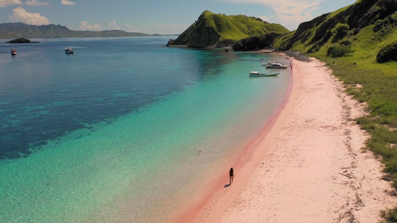 Aerial view of attractive woman walking at pink beach, Padar islands.