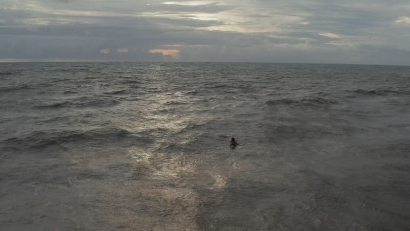 Man floating on the surf board in sea waves on a cloudy day. Surfer lying on the surfboard at evening in the ocean