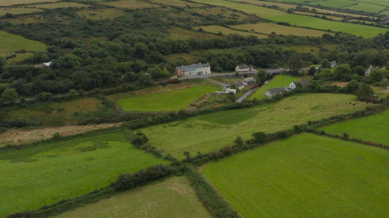 Fly above meadows and pastures in countryside. Tilt up reveal panoramic view with hills in background. Ireland