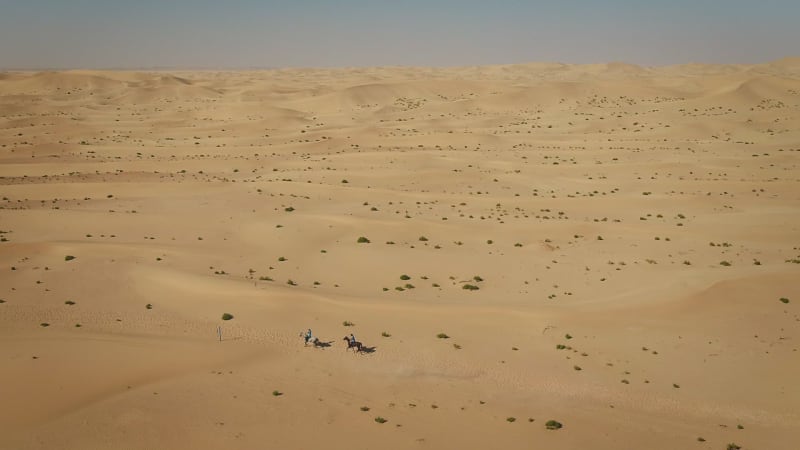 Aerial view of people riding horses in the desert of Al Khatim.