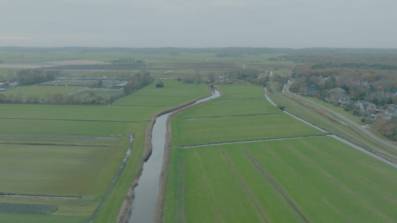 Moving sideways tilt down shot of green farmer fields and water next to the village Bergen in The Netherlands at cloudy daytime.