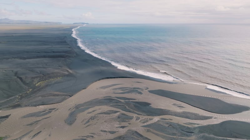 Aerial view of glacial river Jokulsa flowing into sea with black beach, Iceland.