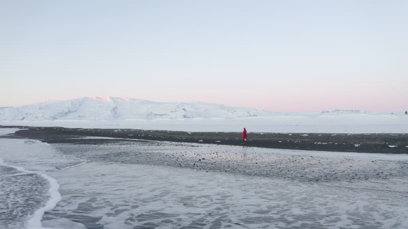 Drone shot of Person walking on Black Beach with white arctic snow in Iceland in Winter Snow, Ice, Waves, Water