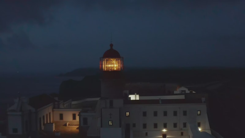 Scenic aerial drone view of lonely lighthouse at sunset dusk, circle pan reveal background sea ocean, Lagos Algarve, Portugal