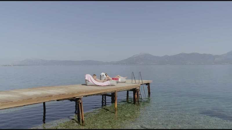 Aerial view passing by two attractive woman sunbathing in Panagopoula.