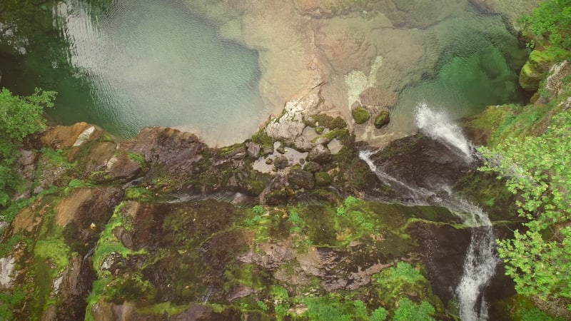 Aerial view of the top of a small waterfall with clean water downhill.