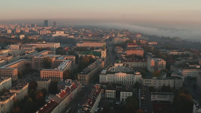 Morning aerial view of buildings in town at sunrise time. Fog around river in background. Warsaw, Poland