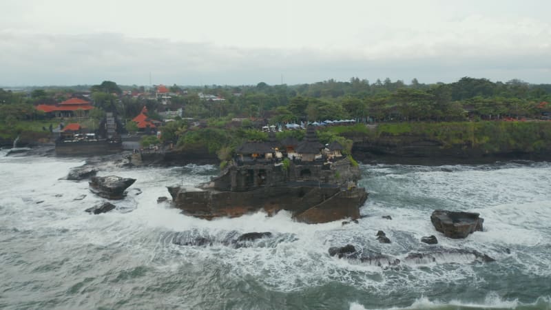 Empty Tanah Lot temple on dark rocky cliff at sea during dangerous weather. Rotating aerial shot of waves crashing ashore the Hindu temple in Bali, Indonesia