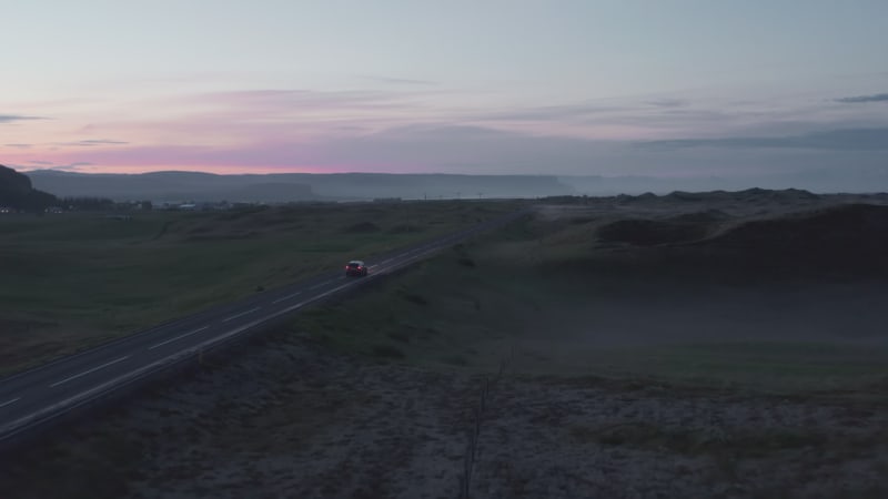 Aerial view of ring road in Iceland with fast driving car at sunset. Top view from drone of highway car peacefully driving at evening. Commercial birds eye drone view