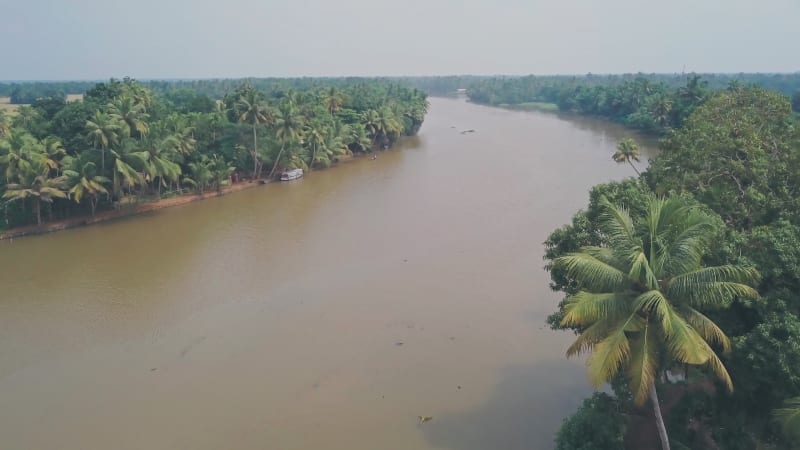 Flying towards brown river surrounded by tropical vegetation in India