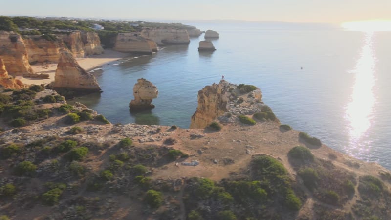 Aerial view of man standing on cliff above arch in Marinha Bay