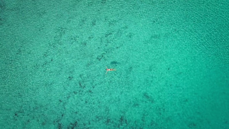 Zoom out aerial view of pregnant woman floating on her back