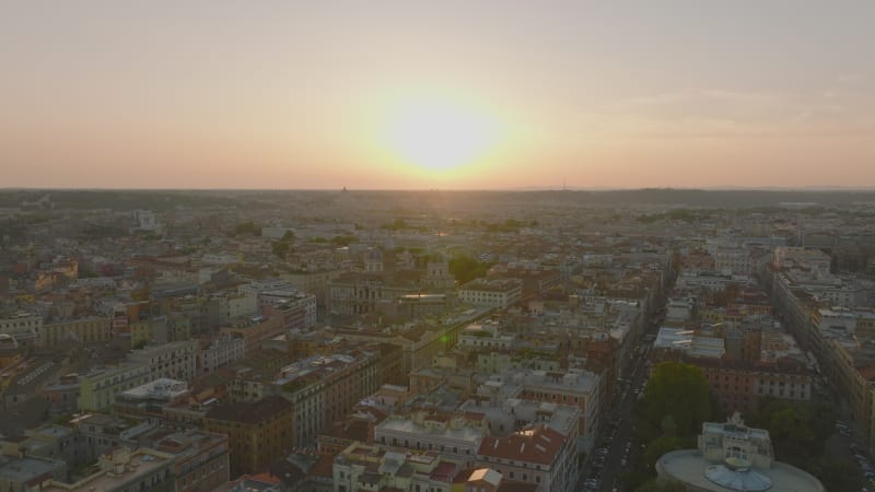 Aerial ascending footage of buildings in large city against romantic sunset sky. Historic landmarks between residential houses. Rome, Italy