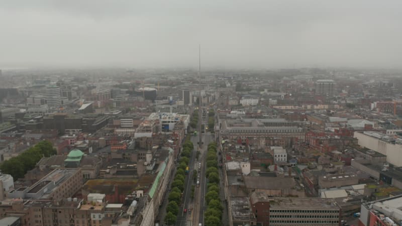 Foggy aerial view of large town. Tilt down footage to wide street and tall steel pinlike Monument of Light. Dublin, Ireland