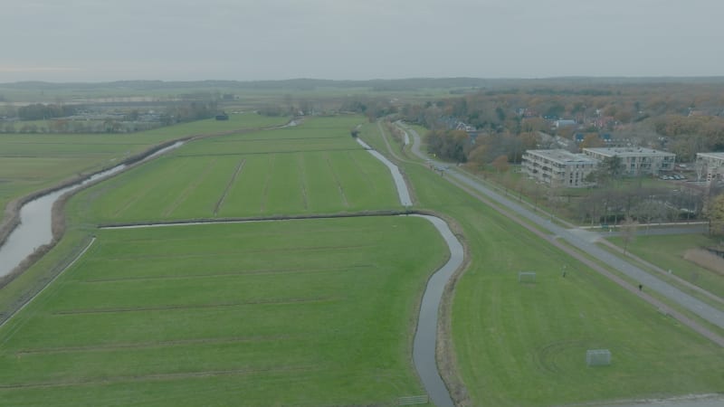 Push in shot of green farmer fields and water next to the village Bergen in The Netherlands at cloudy daytime.