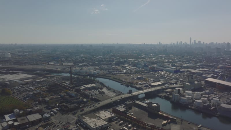 Aerial panoramic footage of city industrial suburbs. Cars driving on bridge over water channel. New York City, USA