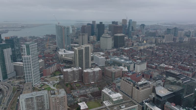 Aerial panoramic footage of city centre and water surface in background. Cityscape with downtown high rise office buildings on cloudy day. Boston, USA