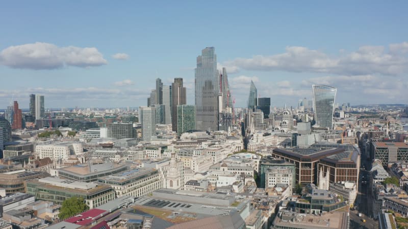 Forwards fly above urban district towards group of glossy glass skyscrapers in City financial hub. London, UK