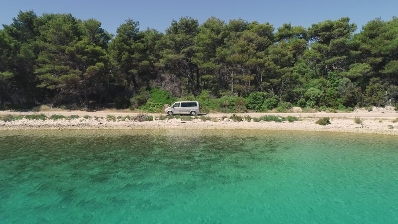 Aerial view of campervan driving near turquoise water