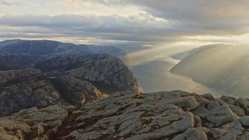 Sunrise light beaming through clouds onto majestic mountains at Preikestolen in Norway.