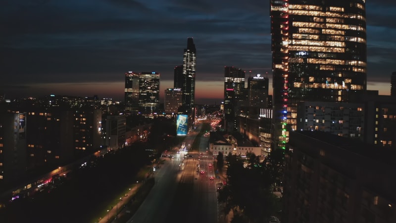 Night city scene, High rise illuminated buildings along wide street. Colourful sunset sky in background. Warsaw, Poland