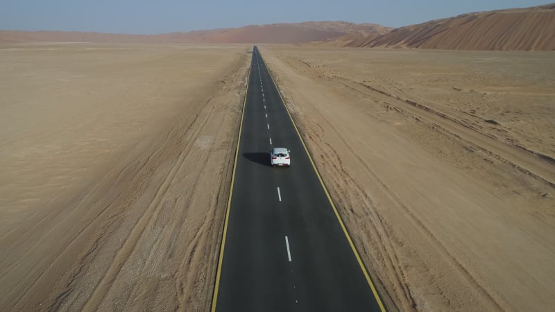 Aerial view of white car in clean road in the desert.