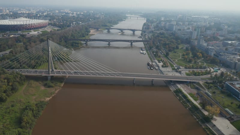 Forwards fly above river. Tilt up reveal row of various bridges connecting bank in city. Modern National stadium on Vistula riverbank. Warsaw, Poland