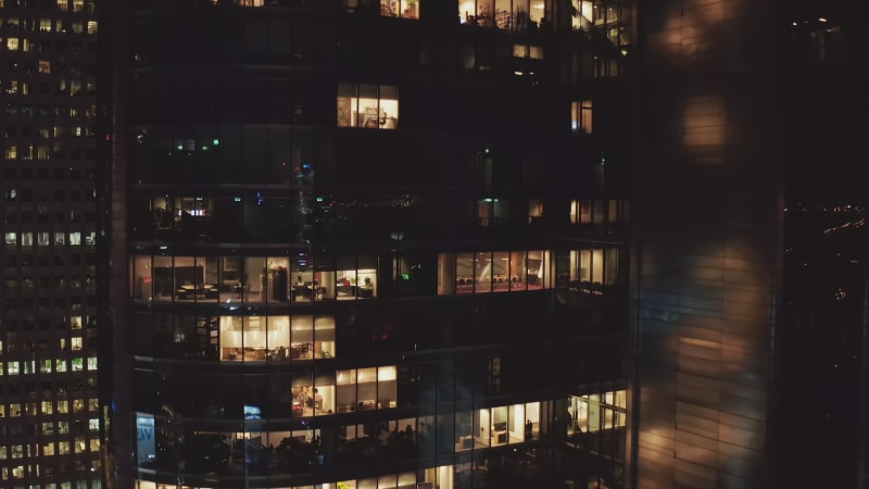 Descending shot of modern high rise building at night. Lighted office windows in late evening. Warsaw, Poland