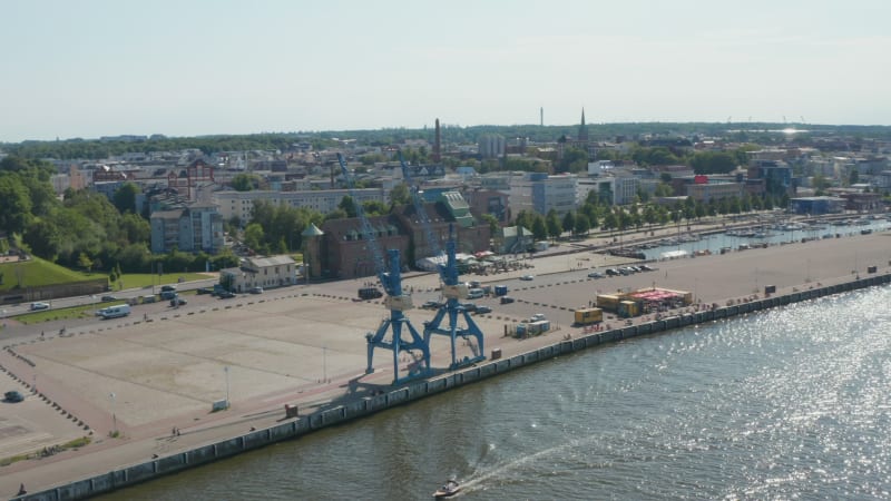 Aerial view of docks with two harbour cranes. Glittering water surface of river. Town in background