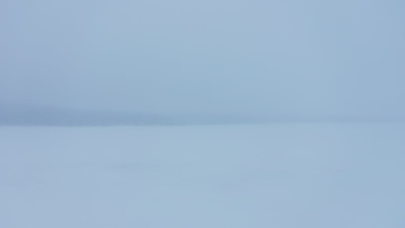 Snow covered frozen lake behind evergreen trees