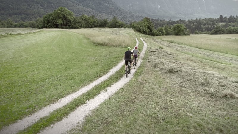 Aerial view of two cyclists riding bike in the forest on dirt road.