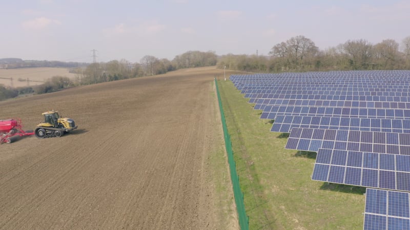 New and Old Farming as a Seed Drill Works Alongside a Solar Power Farm