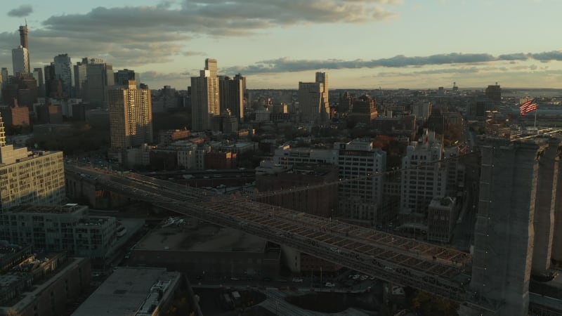 Aerial view of city in sunset time. Busy multilane road leading on old bridge with American flag raises on top. Brooklyn, New York City, USA