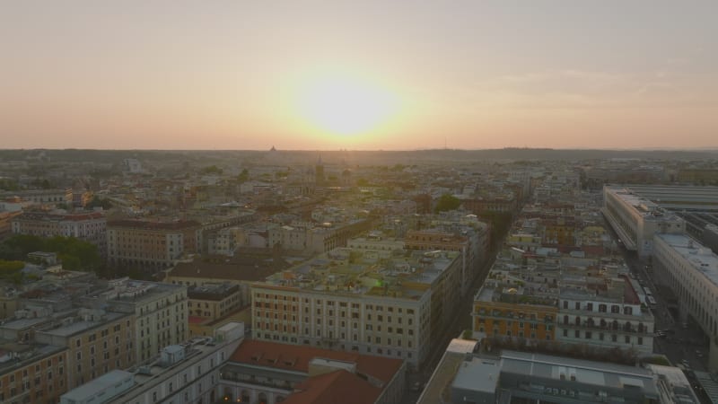 Forwards fly above town development in Esquilino borough. Buildings in large city in flat landscape against sunset. Rome, Italy