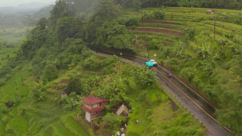 Aerial view of a truck driving on the hill road past farm fields in rural countryside in Bali. Car traffic near rainforest in tropical Asian countryside