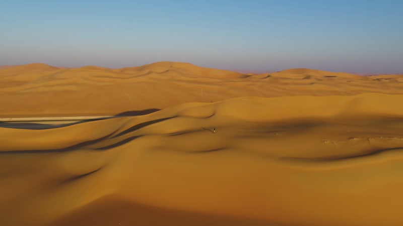 Aerial view of a man walking on dunes during the sunset.