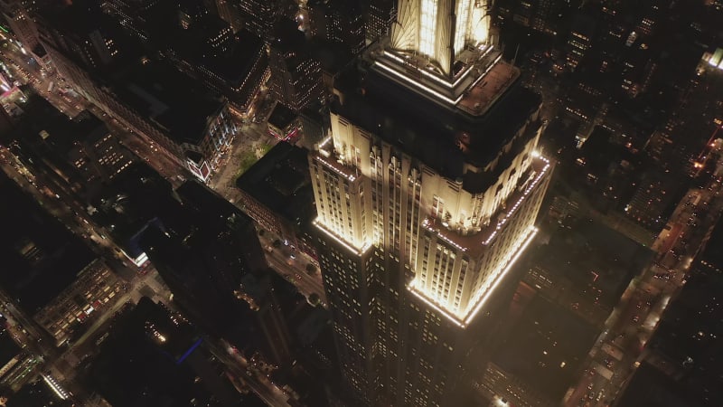 Tournage panoramique lent autour du sommet de l'Empire State Building de nuit. Illumination Aerial du gratte-ciel de Manhattan avec les lumières de la ville vers septembre 2019