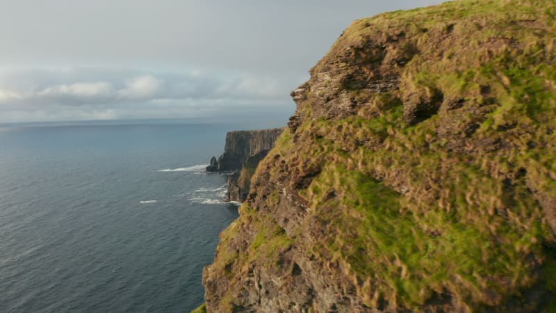 Forwards fly along sea coast. Revealing majestic stone wall lit by late afternoon sun. Cliffs of Moher, Ireland