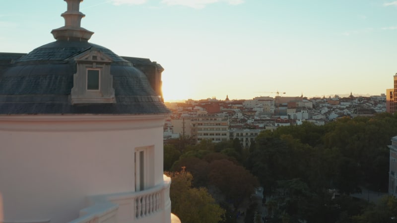 Forwards ascending fly along historic palace. Revealing of cityscape against setting sun.