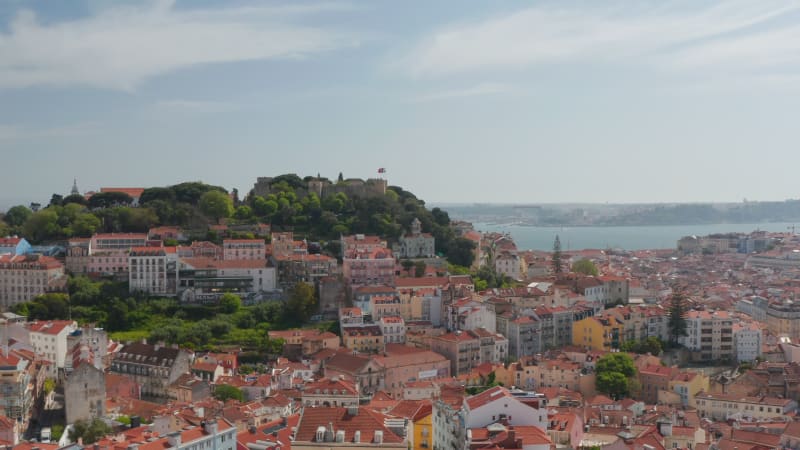 Aerial dolly in view of red rooftops of traditional colorful European buildings and boats at sea off the shore of Lisbon, Portugal