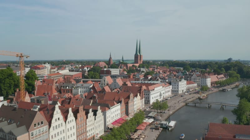 Forward reveal of town houses on wide waterfront. Aerial view of historic city centre. Fly to Luebeck cathedral. Luebeck, Schleswig-Holstein, Germany