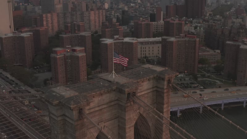 Close up orbit flight over Brooklyn Bridge with Scenic American flag Waving and Boat passing through East River, Aerial View in New York City