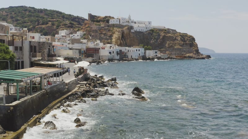 Waves splashing over rocks on sea wall at foot of Greek town in hillside