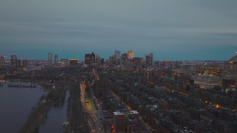 Slider of residential urban neighbourhood on waterfront and illuminated downtown skyscrapers in distance. Boston, USA