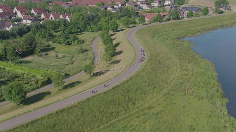 Cycling Team On Dike Road Between River and Houses